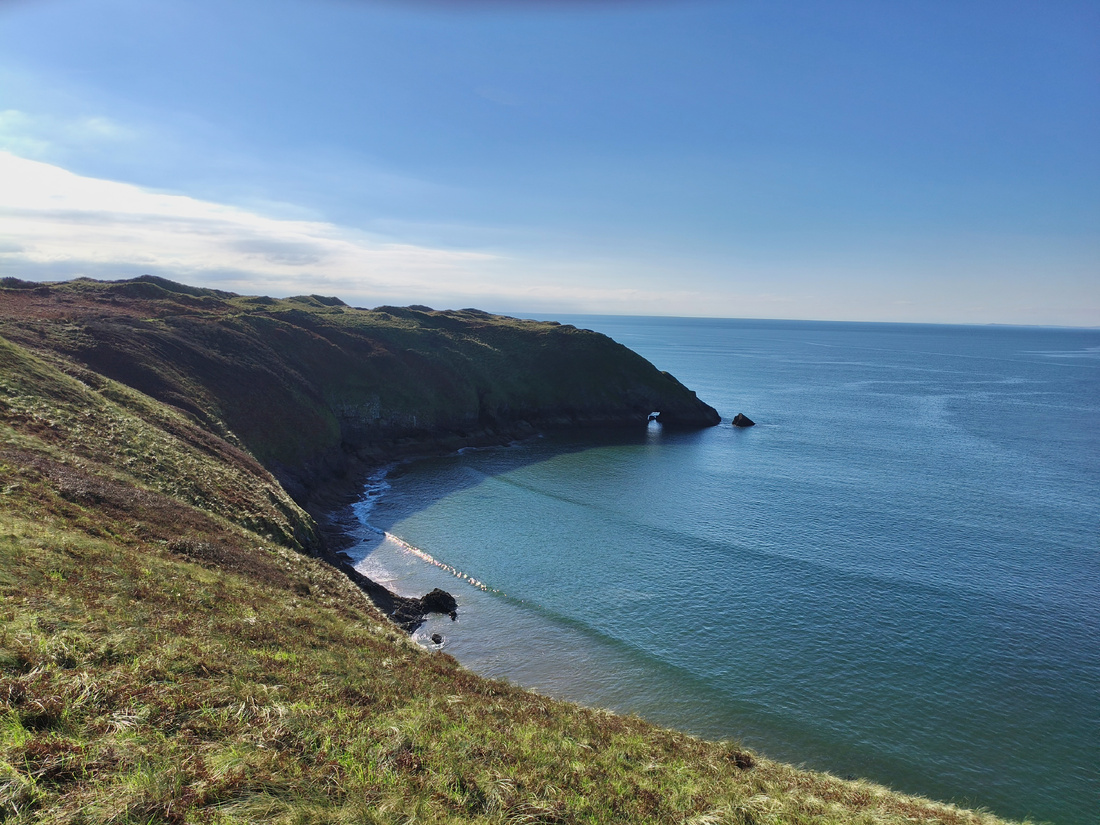 Photographie d’une falaise se jetant dans la mer. La pointe de la falaise forme une sorte de tore, où la mer peut passer.