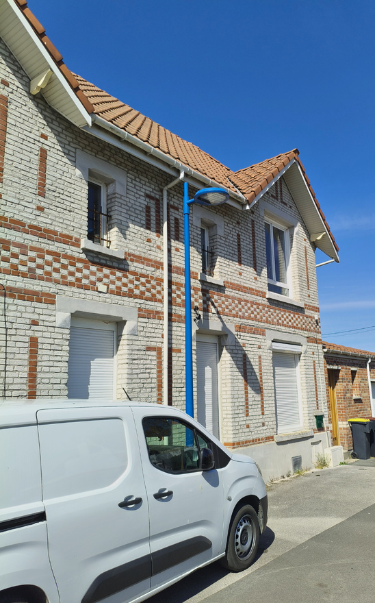 Photographie d’une maison de briques blanches avec des motifs en briques rouges. Au devant, une camionnette et un lampadaire.